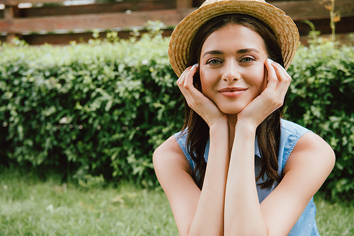 cheerful young woman in straw hat touching face and 