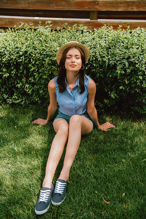 attractive young woman in straw hat sitting on grass