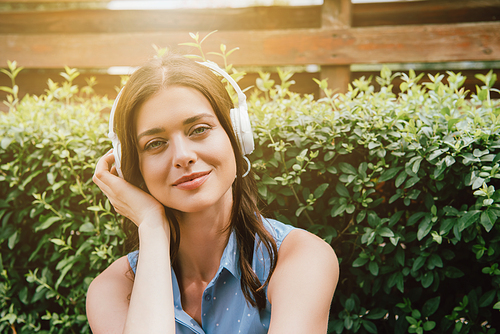 happy woman listening music in wireless headphones near bush