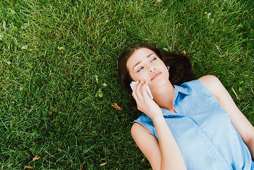 top view of girl lying on green grass and talking on smartphone