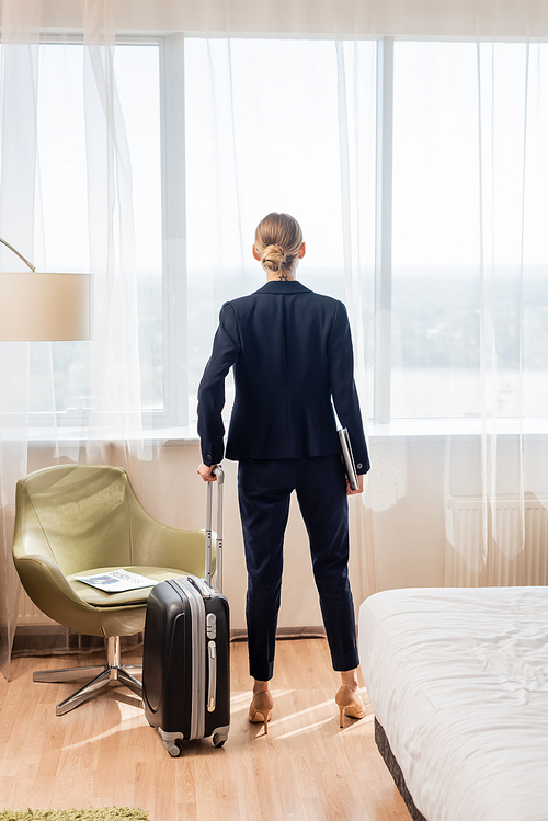 back view of businesswoman standing with laptop and suitcase in hotel room