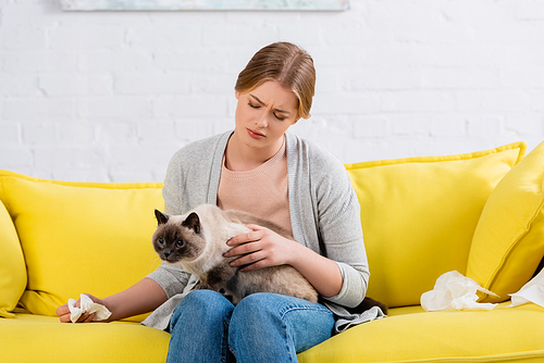 Woman with allergy holding napkin and siamese cat on couch
