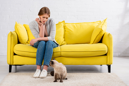Sad woman with allergy holding napkin near cat in living room