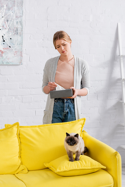 Sad woman holding napkin and box near siamese cat on couch