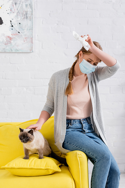 Woman in medical mask suffering from allergy near siamese cat in living room