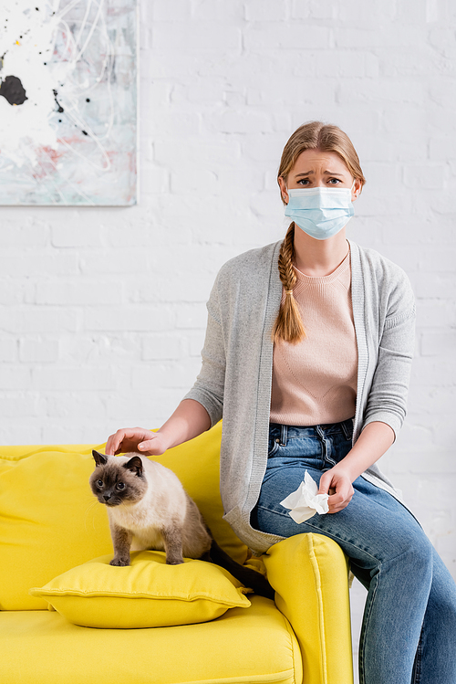 Upset woman in medical mask holding napkin during allergy near siamese cat