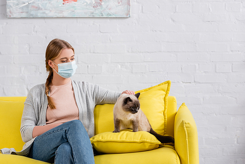 Woman in medical mask suffering from allergy near siamese cat