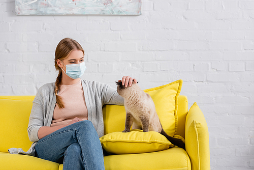 Woman in medical mask stroking siamese cat during allergy