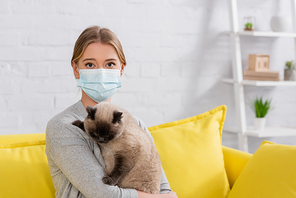 Young woman in medical mask  while holding siamese cat