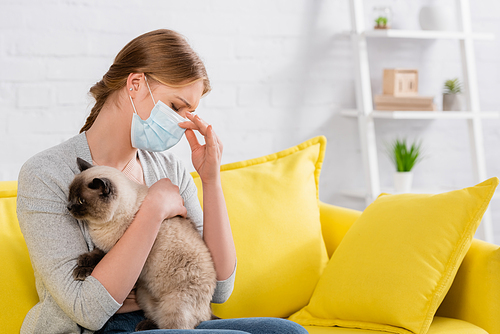 Woman in medical mask holding siamese cat at home