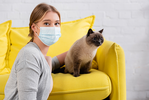 Young woman in medical mask  near siamese cat at home