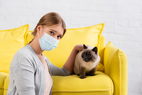 Woman in medical mask petting siamese cat during allergy