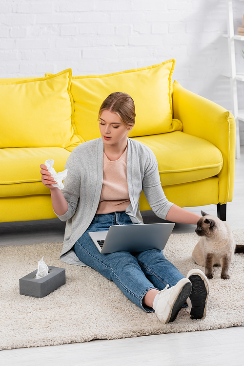 Woman with laptop taking napkin during allergy near siamese cat