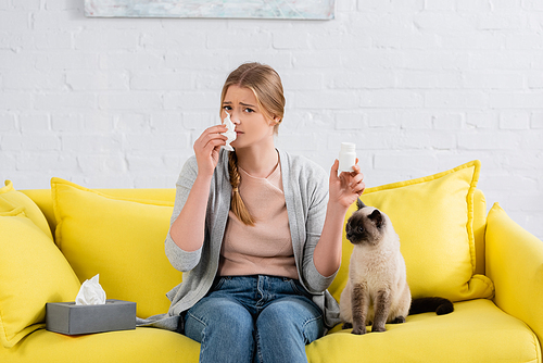 Woman with allergy holding napkin and pills near siamese cat on couch