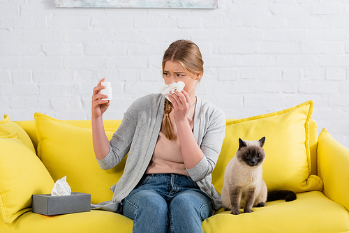 Woman with napkin looking at jar with pills during allergy near siamese cat