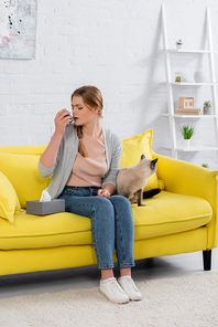 Young woman with allergy using inhaler near napkin and siamese cat