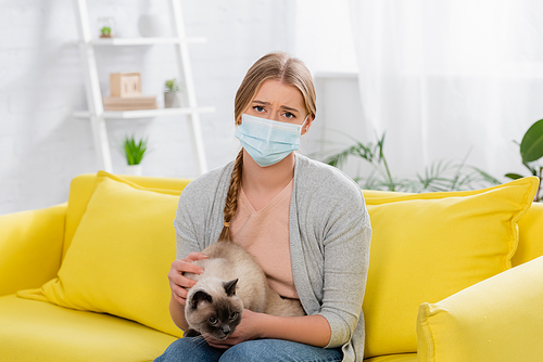 Sad woman in medical mask holding siamese cat on hands during allergy