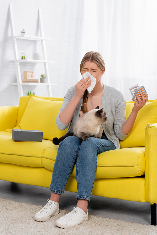 Woman with allergy sneezing while holding pills and siamese cat
