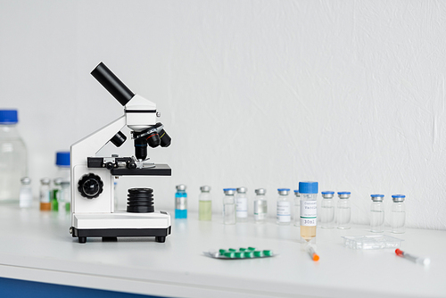 Microscope near vaccines and syringes on blurred foreground in laboratory