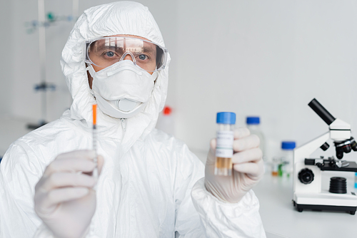 Scientist holding syringe and vaccine on blurred foreground in laboratory