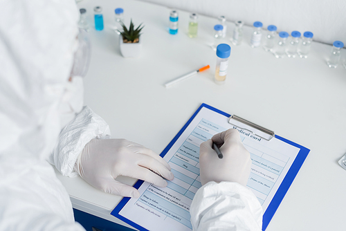 Scientist on blurred foreground writing on medical card near vaccines in laboratory