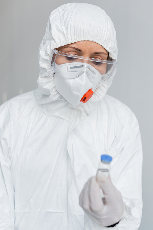 Scientist in goggles and hazmat suit holding vaccine on blurred foreground