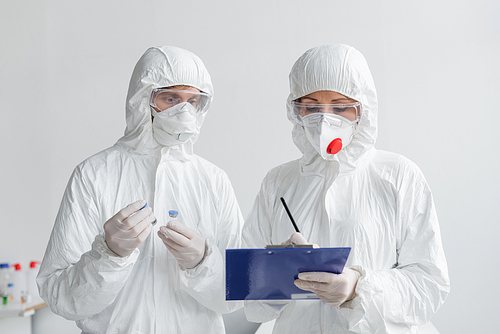 Scientists in hazmat suits working with vaccines and clipboard in laboratory