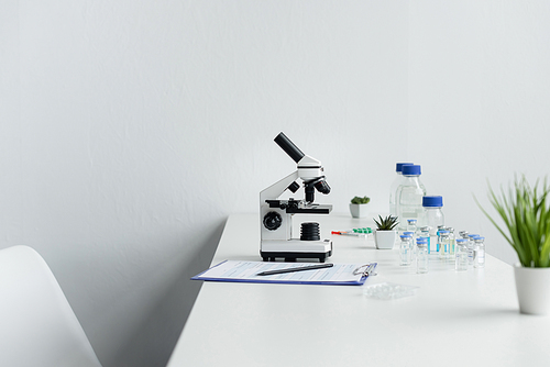 Microscope near vaccines and clipboard on table in laboratory