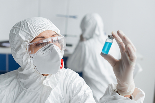 Scientist holding jar with vaccine on blurred foreground while working in laboratory