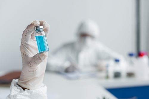 Jar with blue vaccine in hand of scientist in laboratory