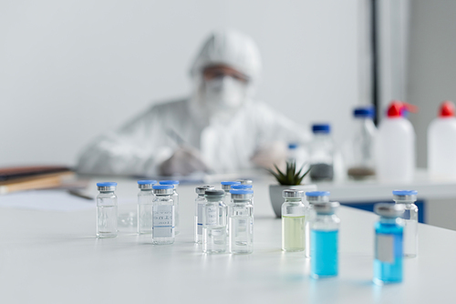Jars with vaccines near scientist working on blurred background