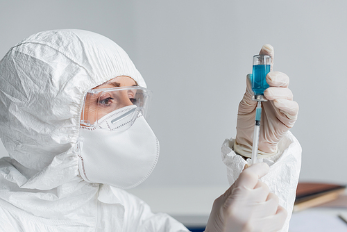 Scientist in protective uniform picking up vaccine in syringe in laboratory