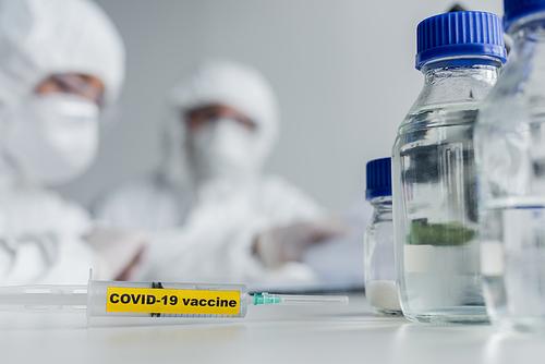 Syringe with covid-19 vaccine lettering near scientists in laboratory