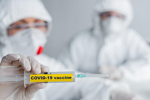 Syringe with covid-19 vaccine lettering in hand of scientist on blurred background