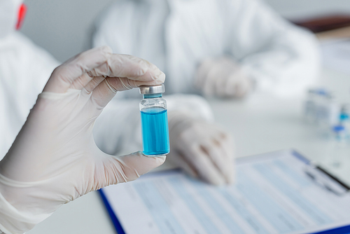 Cropped view of vaccine in hand of scientist on blurred background