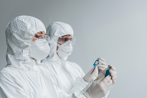 Scientist in hazmat suit and goggles holding vaccine near colleague