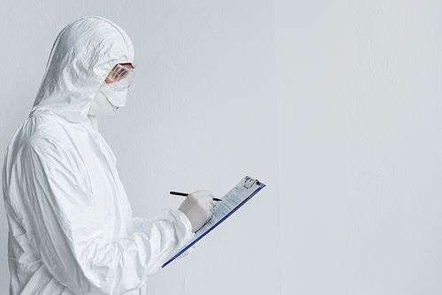 Scientist in protective uniform writing on clipboard