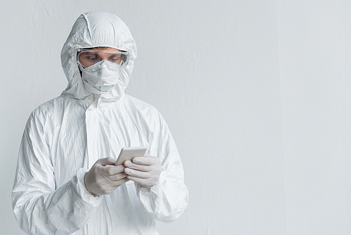 Scientist in hazmat suit using smartphone near wall