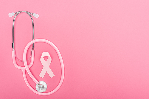 top view of pink stethoscope and breast cancer symbol on pink background with copy space