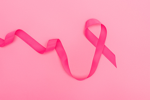 top view of curved crimson breast cancer ribbon on pink background