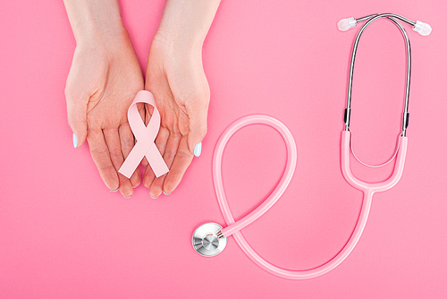 cropped view of woman holding pink breast cancer sign in hands near stethoscope on pink background
