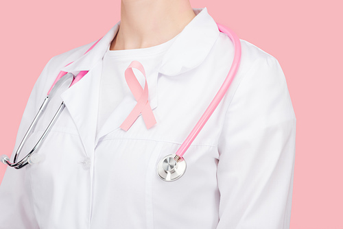 partial view of doctor in white coat with pink breast cancer sign and stethoscope isolated on pink