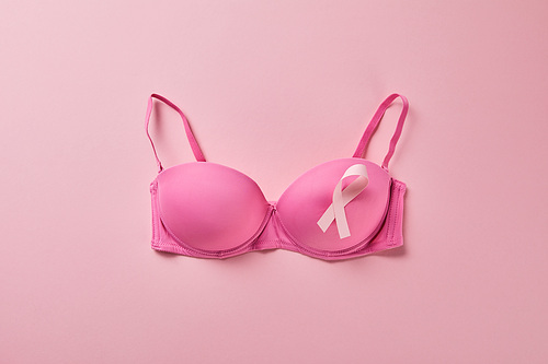 top view of ribbon on brassiere on pink background, breast cancer concept