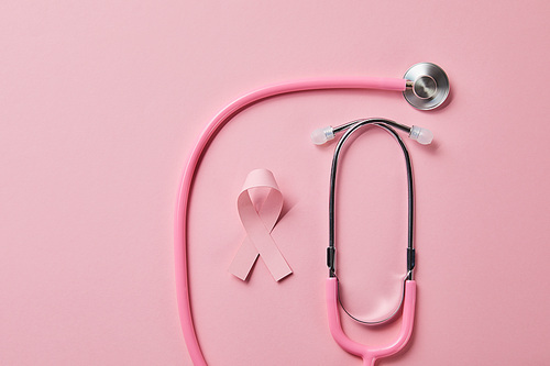 pink stethoscope and breast cancer ribbon on light pink background