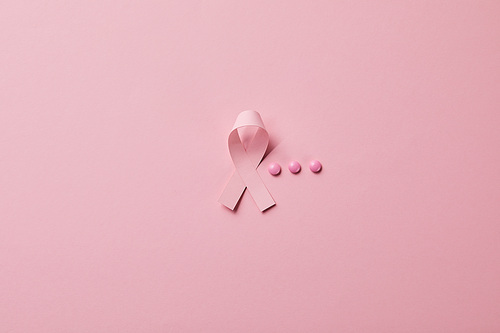 breast cancer ribbon and three pills on light pink background