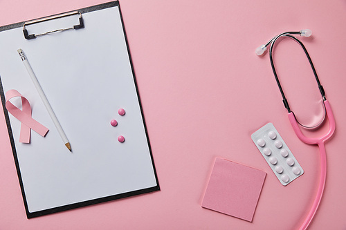 pencil, three pills and breast cancer ribbon on folder with empty paper near stethoscope, blister pack and pice of paper on pink background