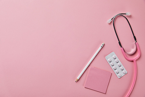 top view of stethoscope, pencil, piece of paper and blister pack on pink background