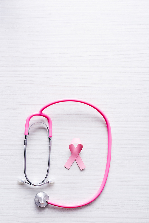 Top view of ribbon of breast cancer awareness and stethoscope on white wooden background