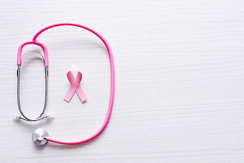 Top view of stethoscope and ribbon of breast cancer awareness on white wooden background