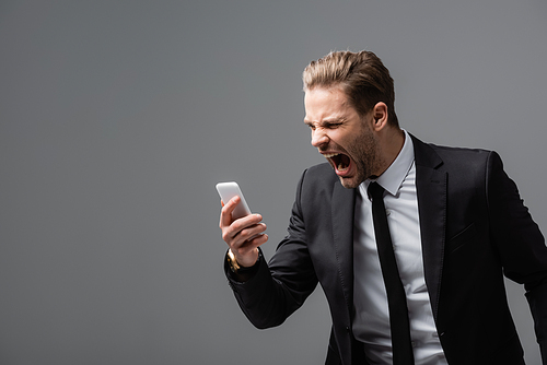 angry businessman screaming during video call on mobile phone isolated on grey